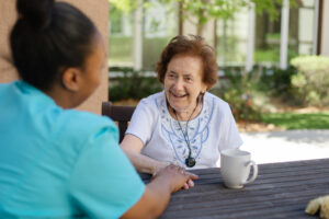 Tuscan Garden’s team member is seated at a table outside with a smiling community resident, having a conversation.
