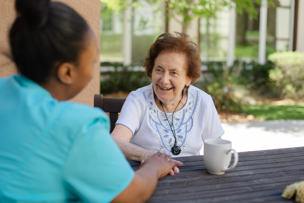 Tuscan Garden’s team member is seated at a table outside with a smiling community resident, having a conversation.