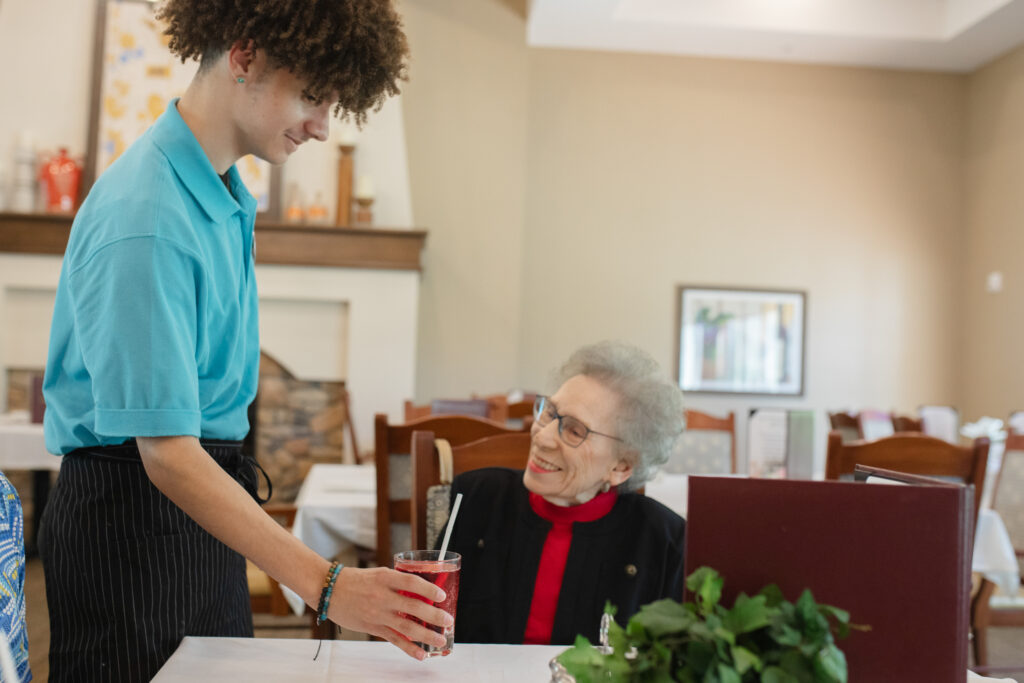 Smiling female resident being served a drink at a senior living community