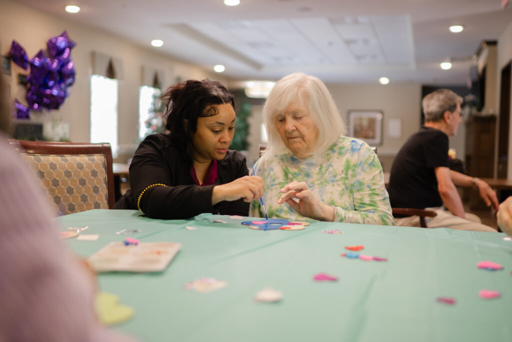 Tuscan Garden’s team member is seated at a table with a smiling community resident, painting