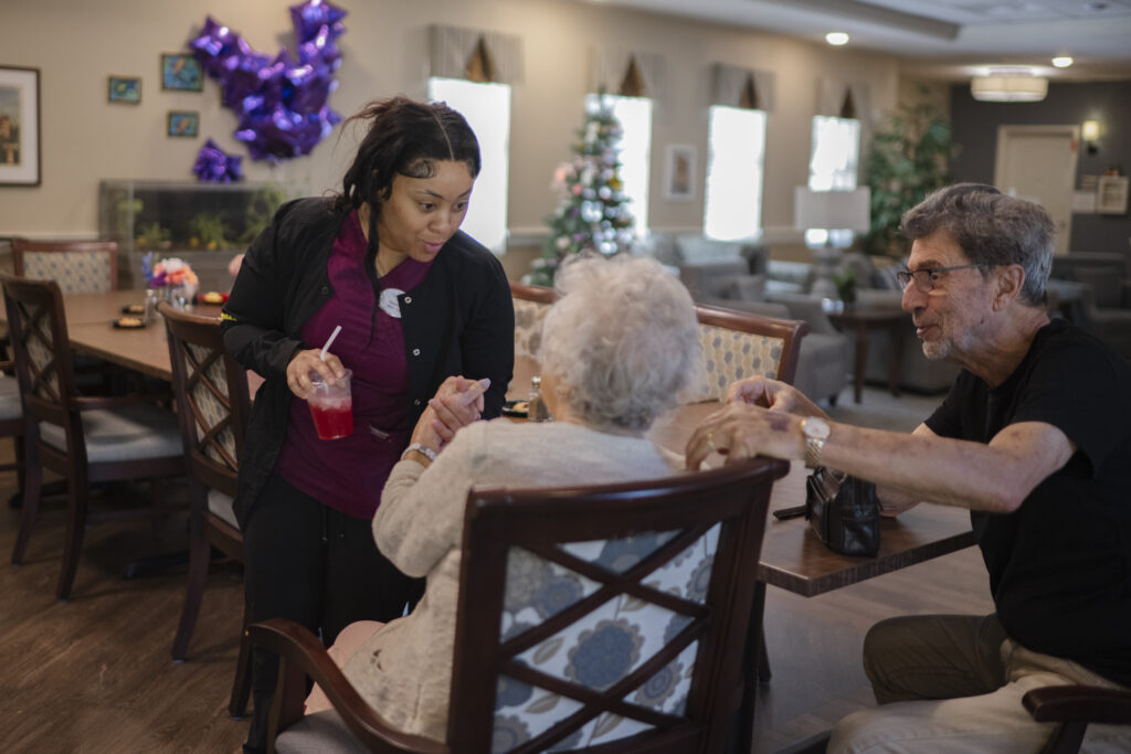 A Tuscan Gardens at Palm Coast associate attentively serves a community resident at a dining room table, showcasing a moment of care and connection.