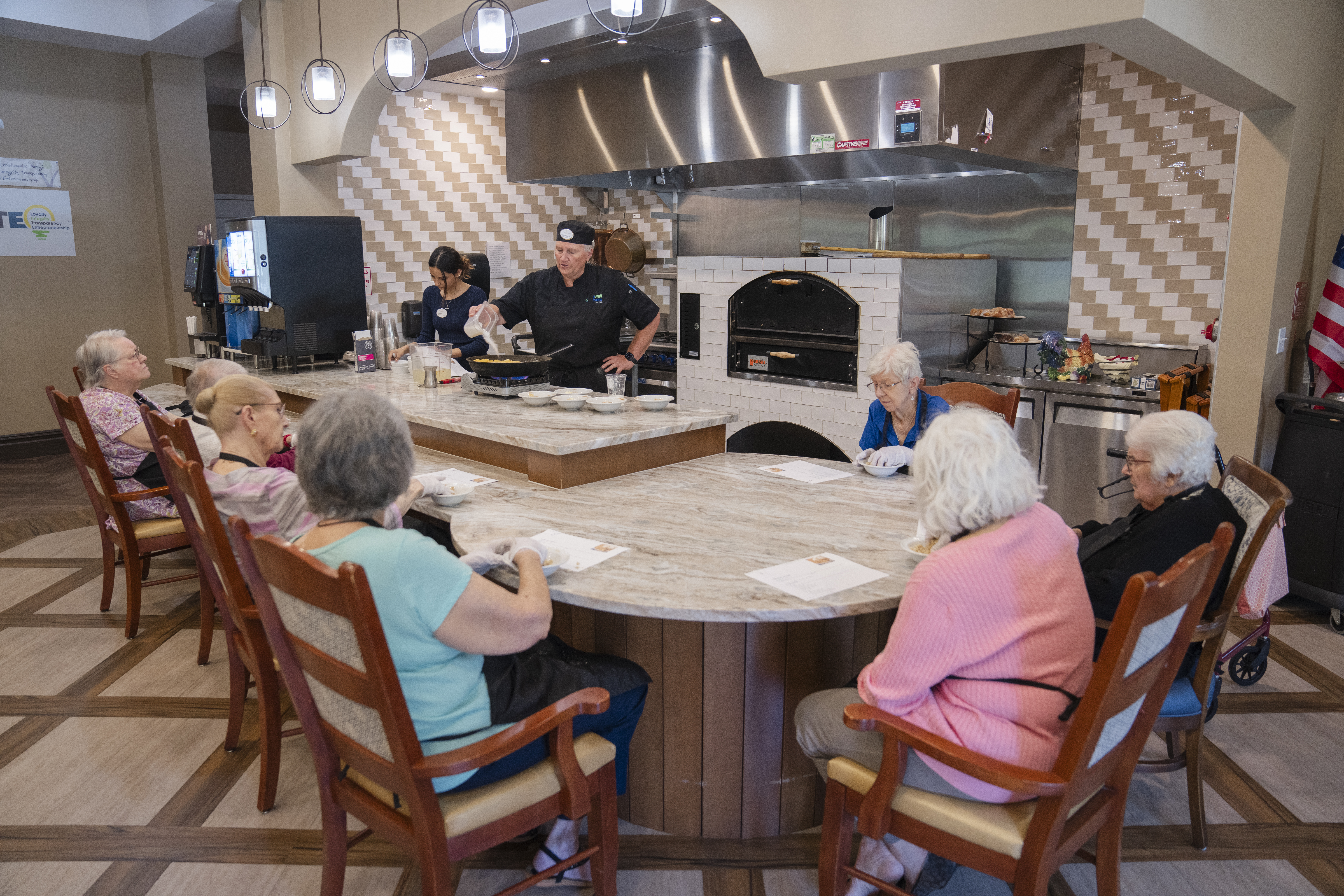 A group of seniors enjoying a cooking demonstration at Tuscan Gardens Senior Living Community