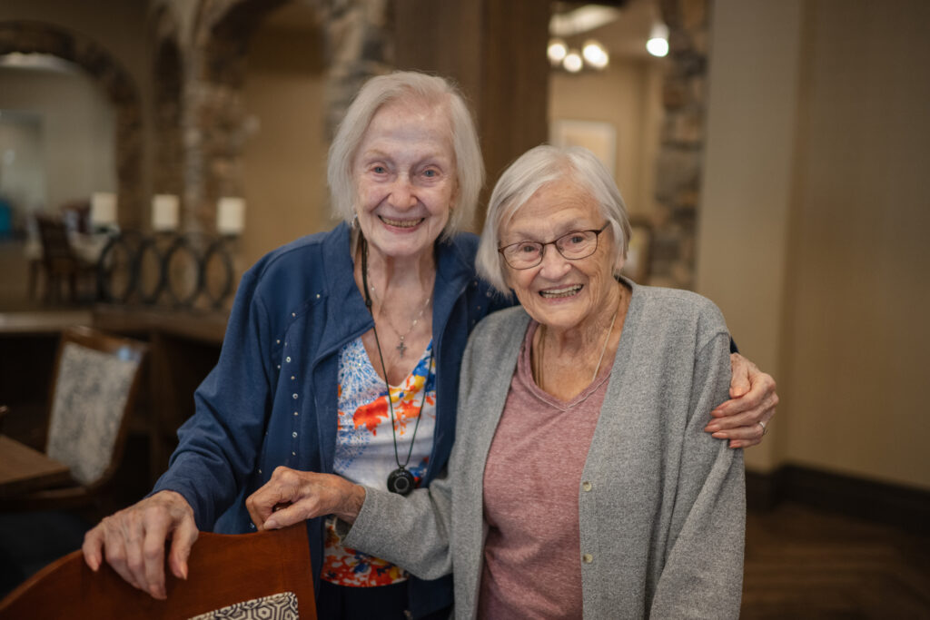 Two senior women community residents smiling and holding each other close.