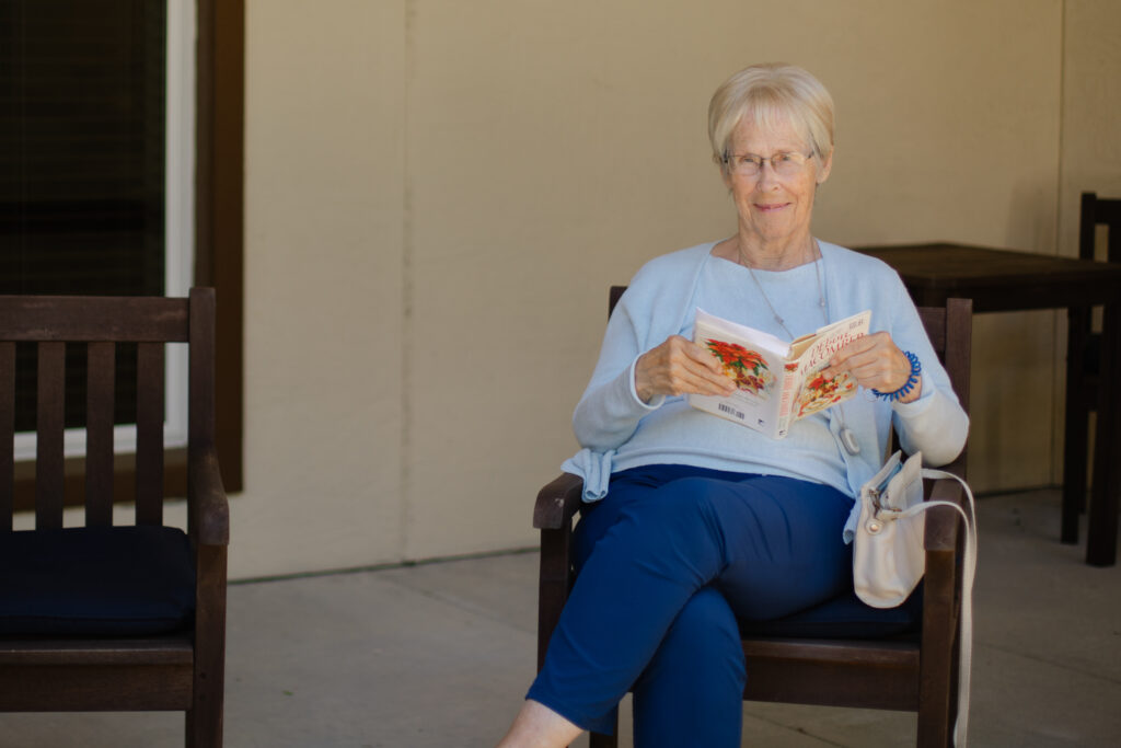 Senior woman sitting reading a book on the patio at Tuscan Gardens