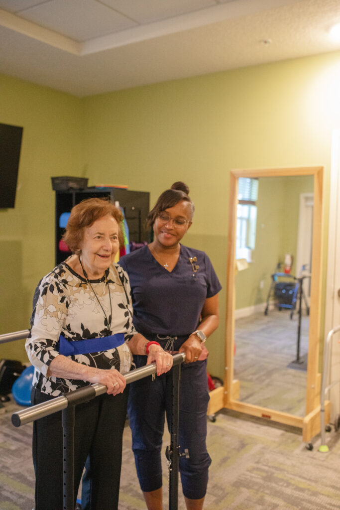 A community resident is happy doing her exercises while being assisted by a Tuscan Gardens of Palm Coast's associate.