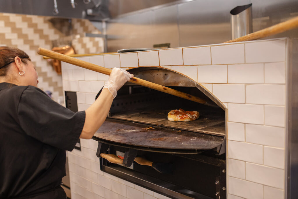 A woman carefully places a pizza into a traditional pizza oven, preparing to cook it to perfection