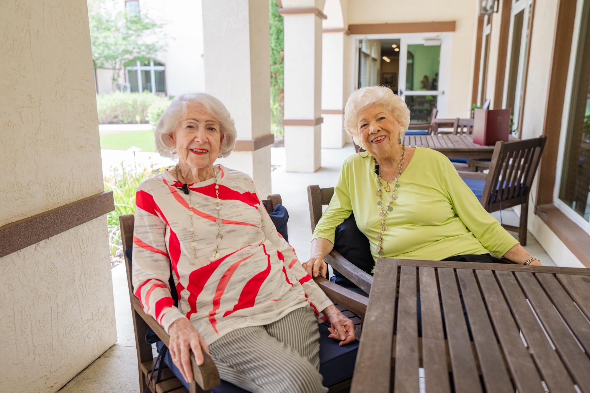 Two women smiling and sitting together outdoors at a Palm Coast senior living community, enjoying a peaceful moment and each other’s company.