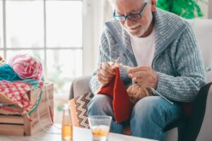 An older man engaging in seasonal activities by knitting a holiday scarf at Tuscan Gardens of Palm Coast